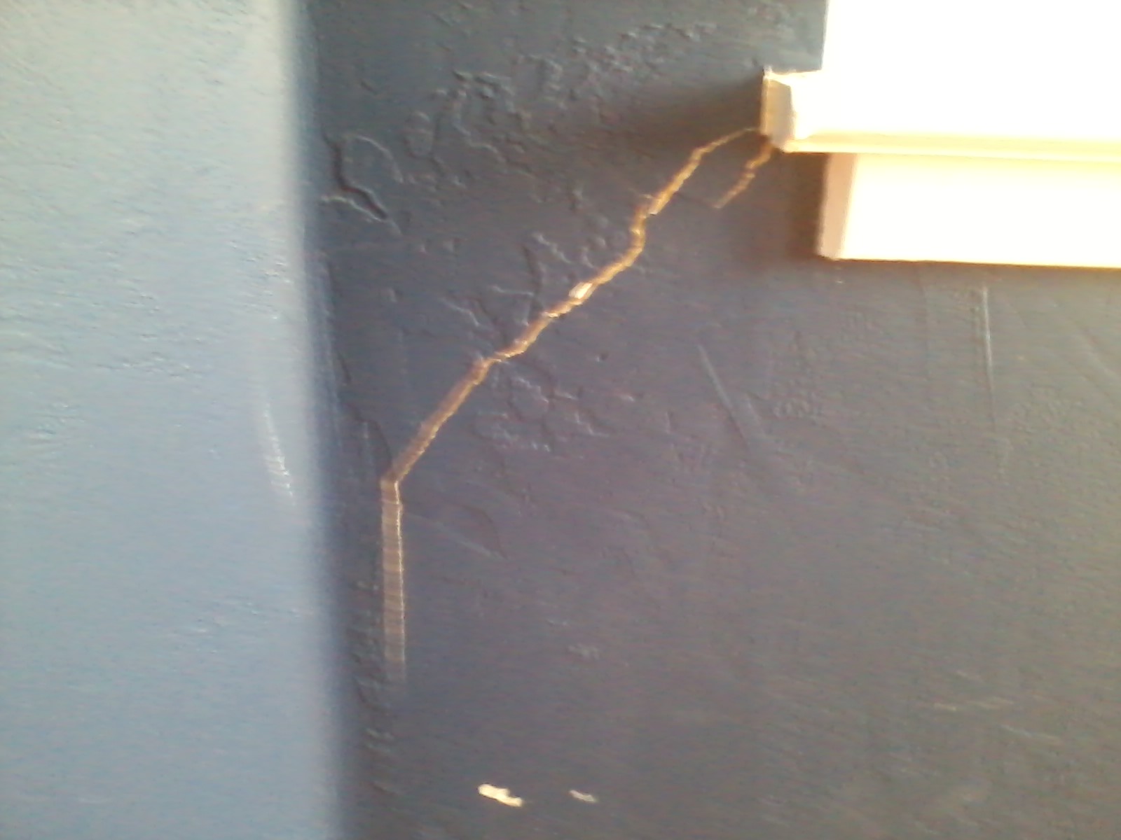 What causes drywall to crack near the corners of doors and windows?